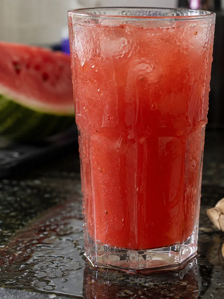 Copo gelado de suco vermelho com gengibre e pimenta ao lado