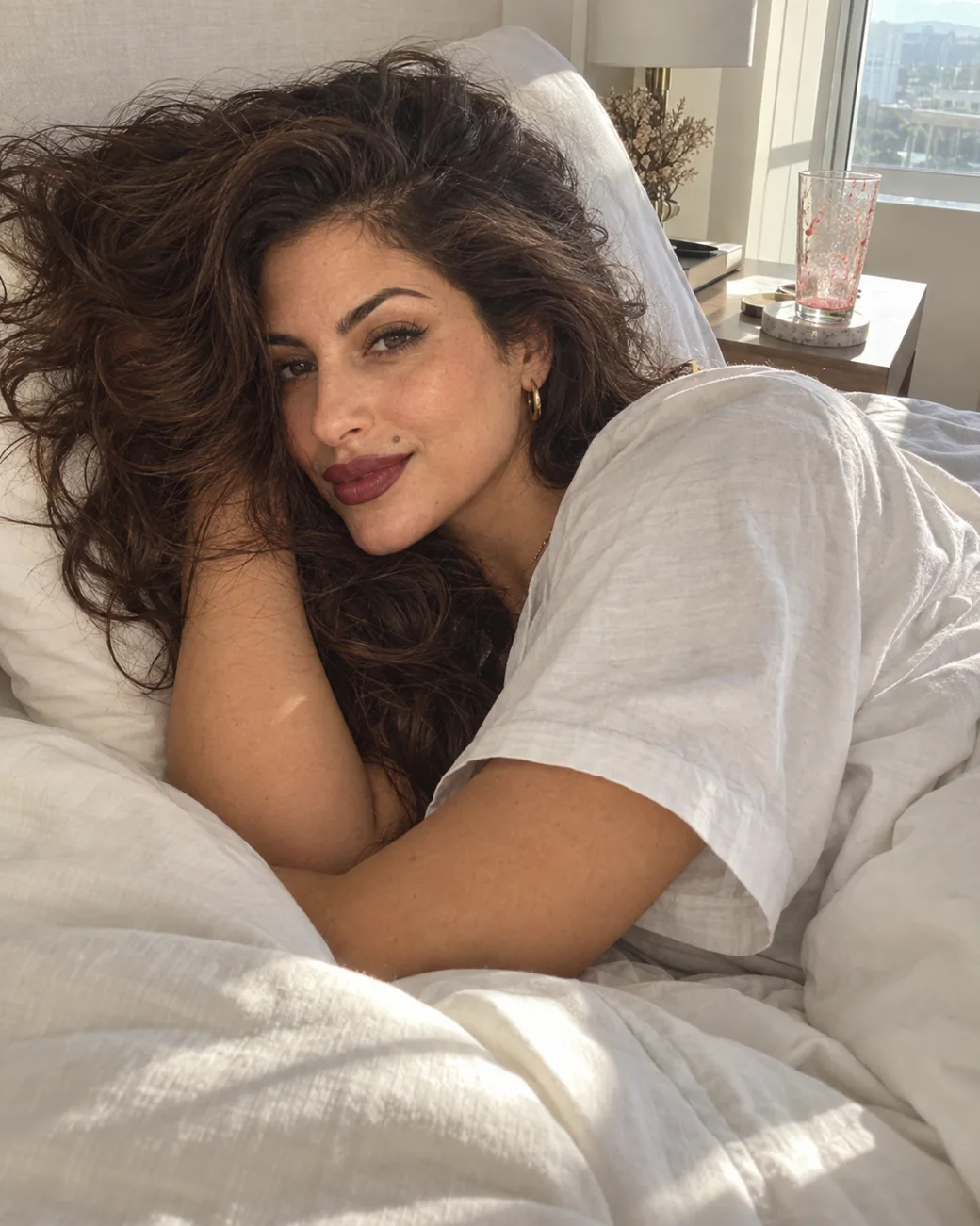 Mulher deitada na cama de manhã, sorrindo, com o cabelo bagunçado
