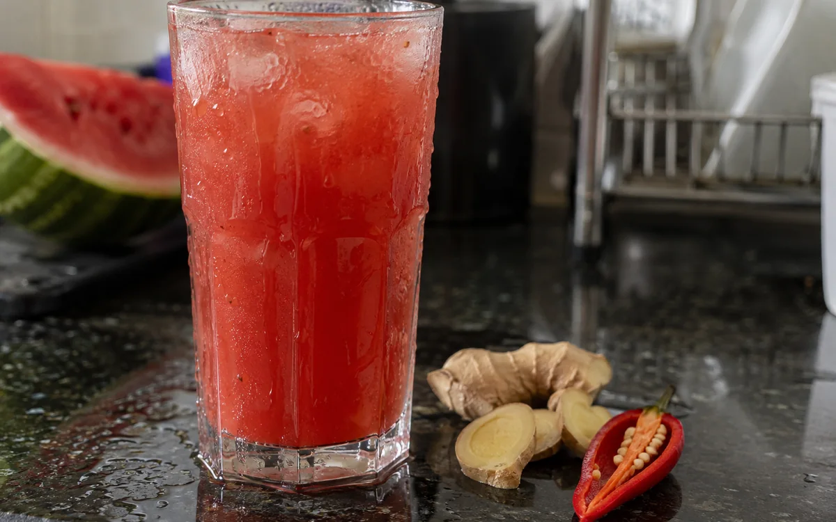 Copo gelado de suco vermelho de gengibre e pimenta, suando na bancada