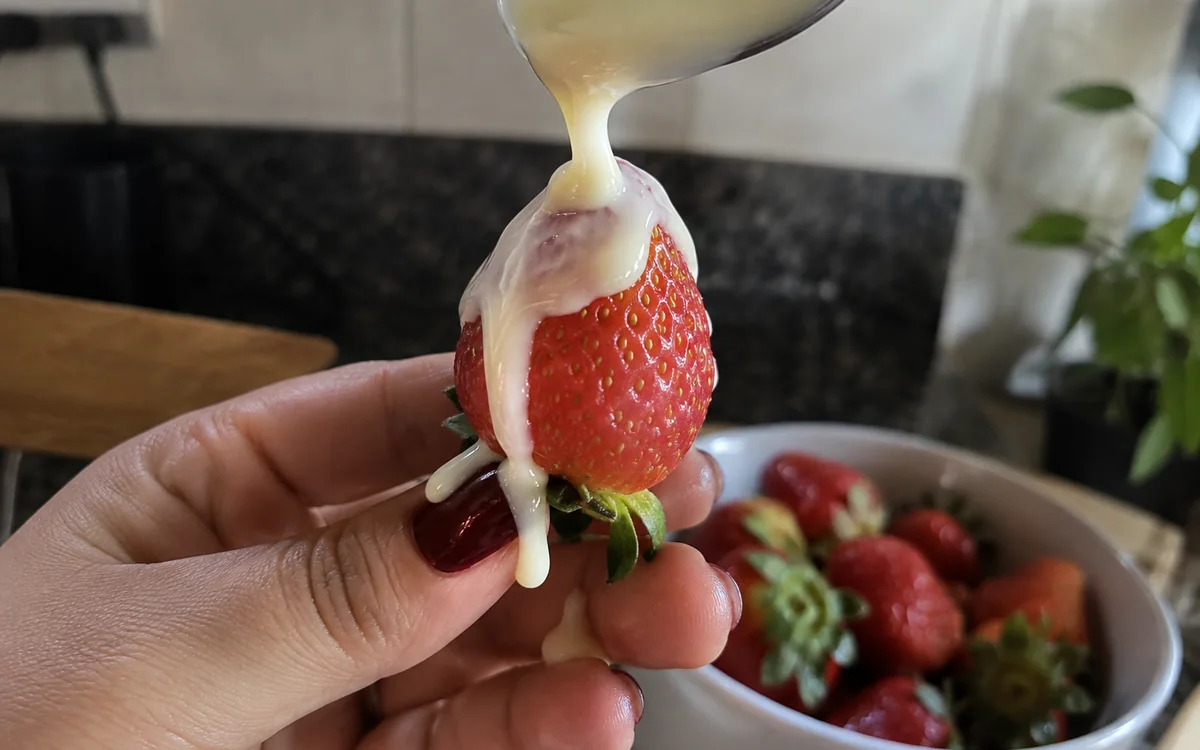 Leite condensado escorrendo de um morango pelos dedos